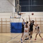 Gracze AZS UJK stoją pod koszem graczy AZS AGH Kraków, zawodnik z Krakowa we fryzurze afro wyciąga rękę w podskoku, aby przejąć piłkę