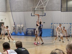 Mateusz Czemerys, zawodnik UJK Kielce, próbuje bronić kosza przed zawodnikiem MKS II Dąbrowa Górnicza, w tle zawodnicy UJK Kielce: od lewej do prawej - Oskar Lesisz, Stanisław Strojek, Norbert Cygan oraz Tymofii Reutov