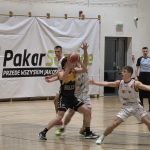Zawodnik Basket Hills Bielsko-Biała usiłuje wykonać rzut na kosz, zawodnik UJK Kielce próbuje odebrać piłkę, za nimi Mateusz Czemerys, a naprzeciw gracza z Basket Hills jeden z braci Strojek