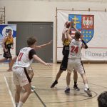 Oskar Lesisz blokuje zawodnika Basket Hills Bielsko-Biała przez rzutem pod kosz UJK Kielce, w tle zawodnicy drużyny gości oraz Dominik Wesołek, a po lewej jeden z braci Strojek